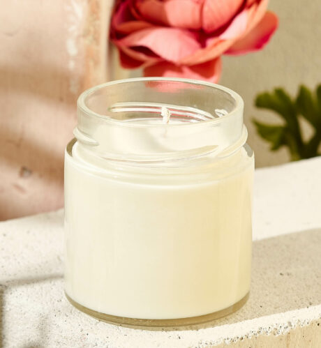 Composition with aromatic candle in jar on concrete podium. Mockup soy wax candle in natural style with flower. Scented handmade candle with wick.  Handmade spa product  from soy wax in glass